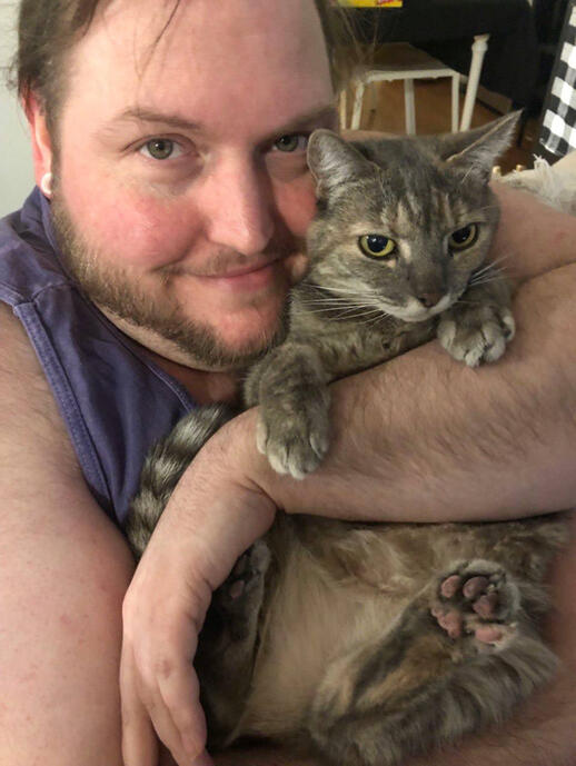A photo of the artist holding a grey/brown tabby cat.